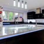 Large striking feature island in black gloss with marble effect quartz worktop and handle trim LED lighting framed by bubble tube pendant lighting above.