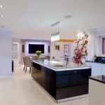 Two tone gloss handless kitchen with stainless steel trim, complimented by black granite worktop and upstands, with a contrasting marble effect quartz worktop on the island giving the ultimate show factor.