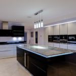 Smoked glass LED light up lift up wall units situated in a sleek modern handless kitchen design using a monochrome colour scheme softened by pale lilac walls.
