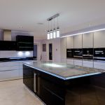 Smoked glass LED light up lift up wall units situated in a sleek modern handless kitchen design using a monochrome colour scheme softened by pale lilac walls.