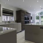 Open plan kitchen dinner fitted with a modern handless matt cashmere and wood effect door comination. Paired with white sparkle quartz worktop, upstand, and matching windowcill.