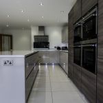Open plan kitchen dinner fitted with a modern handless matt cashmere and wood effect door comination. Paired with white sparkle quartz worktop, upstand, and matching windowcill.